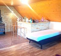 Interiér chaty s krbem, barovým pultem a podlahou s dřevěným dekorem.