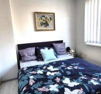 Ložnice v 2pokojovém bytě s postelí, obrazem a zrcadlovou skříní.