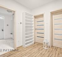 Interiér rodinného domu s podlahou s dřevěným dekorem, dveřmi a bílým regálem.