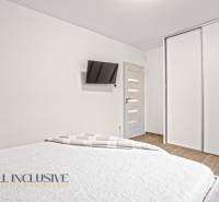 Ložnice v rodinném domě s bílými skříněmi, TV na stěně a podlahou s dřevěným dekorem.