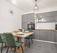 Kuchyně v rodinném domě s šedou linkou, jídelním stolem a zelenými židlemi.