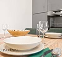 Jídelní stůl s prostíráním a sklenicemi, v pozadí kuchyně v rodinném domě.