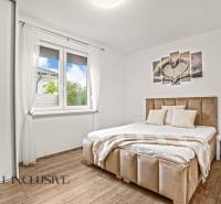 Ložnice se světlým rámem postele, podlahou s dřevěným dekorem a nástěnným obrazem v rodinném domě.