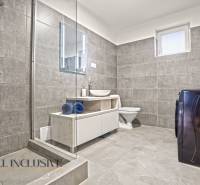 Koupelna v rodinném domě s dlaždicemi, sprchou, pračkou a umyvadlem.