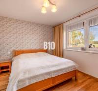 Ložnice v rodinném domě s květovanou tapetou a podlahou s dřevěným dekorem.