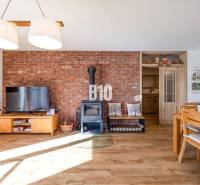 Interiér rodinného domu s cihlovou stěnou, kamny a podlahou s dřevěným dekorem.