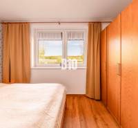 Ložnice v rodinném domě s podlahou s dřevěným dekorem a výhledem z okna.