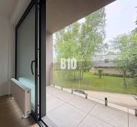 Balkon 2pokojového bytu s výhledem na zeleň a proskleným zábradlím.