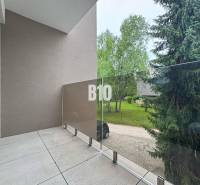 Balkon se skleněným zábradlím nabízející výhled na zeleň v 2pokojovém bytě.