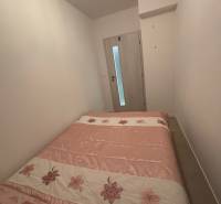 Ložnice v dvoupokojovém bytě s postelí s květinovým motivem a světlými stěnami.