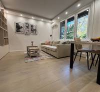 Obývací pokoj ve 2pokojovém bytě, velká sedačka, stolek, podlaha s dřevěným dekorem.