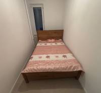 Úzká ložnice v 2-pokojovém bytě s dřevěnou postelí a květinovým přehozem.