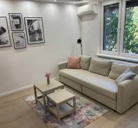 Obývací pokoj v 2-pokojovém bytě, s pohovkou, stolky a fotografiemi na stěně.