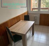 Jídelní kout v 2-pokojovém bytě s dřevěným dekorem na stěnách a dlažbou.