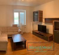 Obývací pokoj s béžovou sedačkou, dřevěným nábytkem a podlahou s dřevěným dekorem.