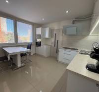 Kuchyně 3pokojového bytu s velkými okny, jídelním stolem a světlou podlahou.