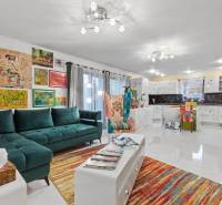 Barevný obývací pokoj v rodinném domě s pohovkou, křeslem a uměním na stěnách.