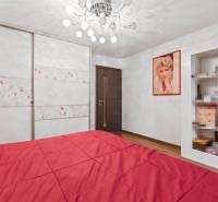 Ložnice rodinného domu s červenou postelí, podlahou s dřevěným dekorem a šatníkem.