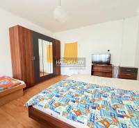 Pokoj s postelí, skříní, televizorem a podlahou s dřevěným dekorem, typický pro hotely a penziony.