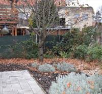 Zahrada u rodinného domu v Nitře, se stromy, trvalkami a dlážděnou plochou.