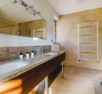 Koupelna v rodinném domě s kamenným umyvadlem, zrcadlem a velkým oknem.