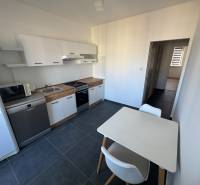 Kuchyně v 3-pokojovém bytě s bílými skříňkami a stolem, na tmavé podlaze.