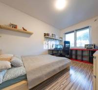 Ložnice v rodinném domě s pracovním stolem, policemi a podlahou s dřevěným dekorem.