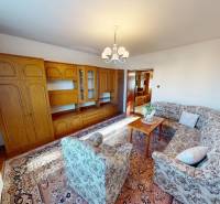 Obývací pokoj v rodinném domě s dřevěnou obývací stěnou a vzorovanou sedací soupravou.