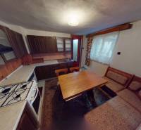 Kuchyně v rodinném domě s dřevěnými skříňkami, sporákem a jídelním stolem.