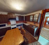 Kuchyně v rodinném domě s dřevěným nábytkem, stolem a spotřebiči.