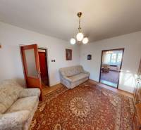 Obývací pokoj rodinného domu s barevným kobercem, pohovkami a dřevěnou obývací stěnou.