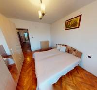 Ložnice s postelí, skříní a podlahou s dřevěným dekorem v rodinném domě.