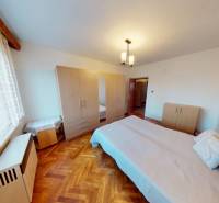 Ložnice v rodinném domě s postelí a skříní, podlaha s dřevěným dekorem.