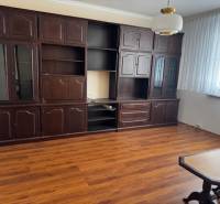 Obývací pokoj v 3-pokojovém bytě s podlahou s dřevěným dekorem, tmavý nábytek.