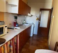 Kuchyně v 3-pokojovém bytě s podlahou s dřevěným dekorem, bílé skříňky, jídelní stůl.