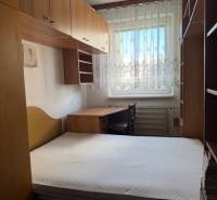 Ložnice v 3-pokojovém bytě s postelí, skříněmi a oknem s krajkovými záclonami.