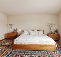 Ložnice v rodinném domě s postelí, nočními stolky a barevným kobercem.