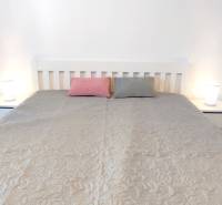 Ložnice s postelí, dvěma polštáři a nočními stolky v dvoupokojovém bytě.