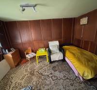 Pokoj se židlemi, lůžkem, skříňkou a dekorativním kobercem v Zahradách.