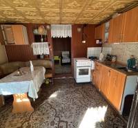 Kuchyně se starším nábytkem, podlaha s dřevěným dekorem, viditelná jídelní část.