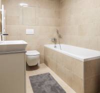 Koupelna v 1-pokojovém bytě s vanou, pračkou a toaletou v neutrálních tónech.