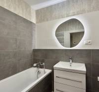 Koupelna v 2-pokojovém bytě s vanou a umyvadlem, světlé a tmavé obklady.