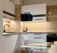 Kuchyně v 2pokojovém bytě s bílými skříňkami, černým dřezem a podlahou s dřevěným dekorem.