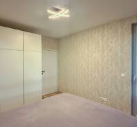 Ložnice v 2-pokojovém bytě s velkou skříní a balkónovými dveřmi.