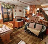 Interiér chaty s pohovkou, podlahou s dřevěným dekorem, jídelním stolem a schodištěm.