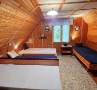 Dřevěný interiér chaty se třemi jednolůžkovými postelemi a krajinomalbou.