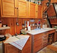 Kuchyně v chatě s dřevěnými skříňkami a bílou pracovní deskou, útulná atmosféra.