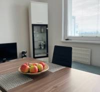 Jídelní stůl s mísou jablek, židle, skleněná vitrína, okno.