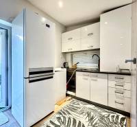 Kuchyně v rodinném domě s bílými skříňkami, velkou lednicí a kobercem s listovým vzorem.