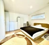 Ložnice v rodinném domě s postelí, skříňkami a podlahou s dřevěným dekorem.